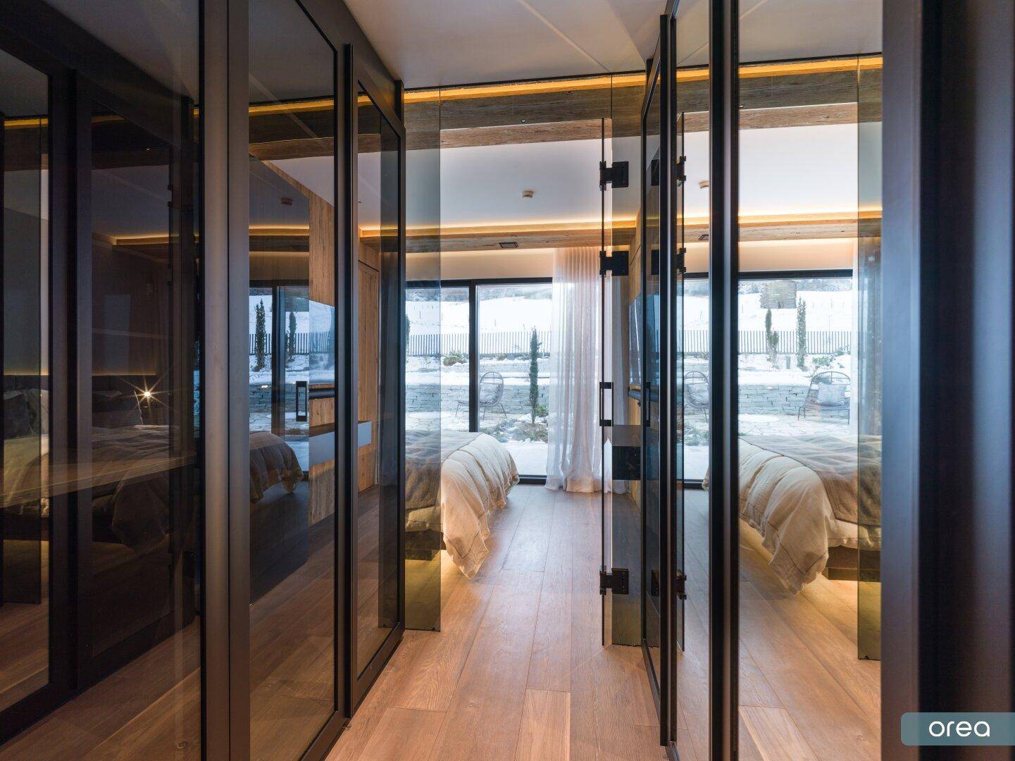 Schlafzimmer mit begehbarem Kleiderschrank und großen Fenstern, die viel Tageslicht hereinlassen.