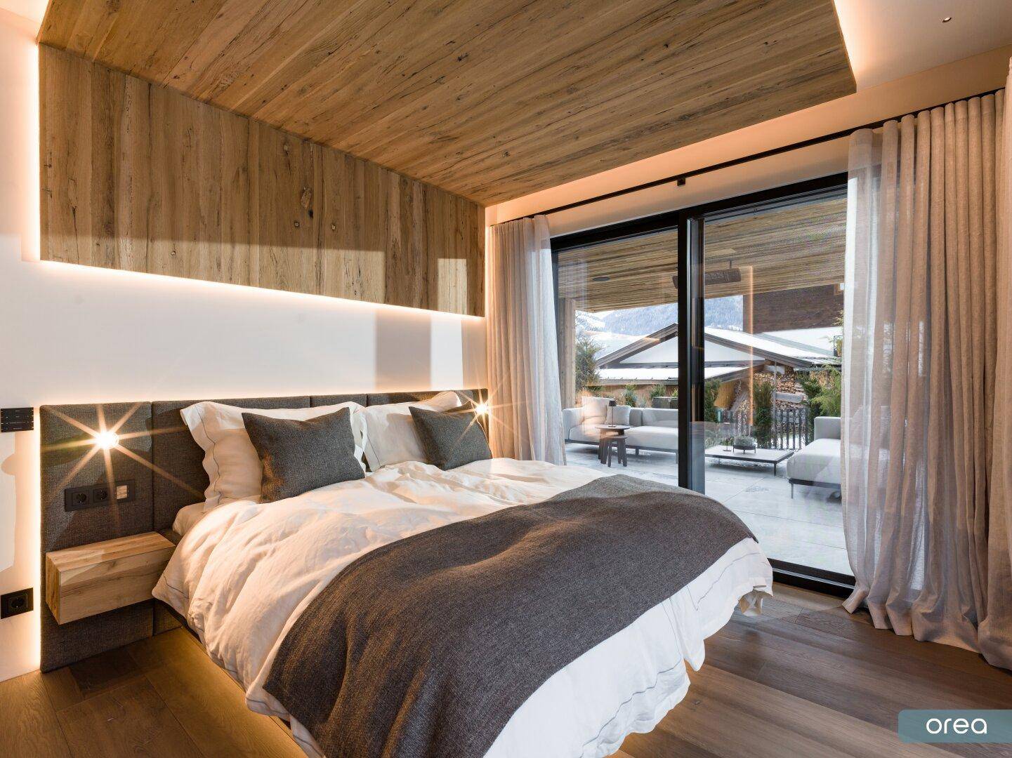 Helles Schlafzimmer mit Zugang zur Terrasse, Holzboden und indirekter Deckenbeleuchtung.