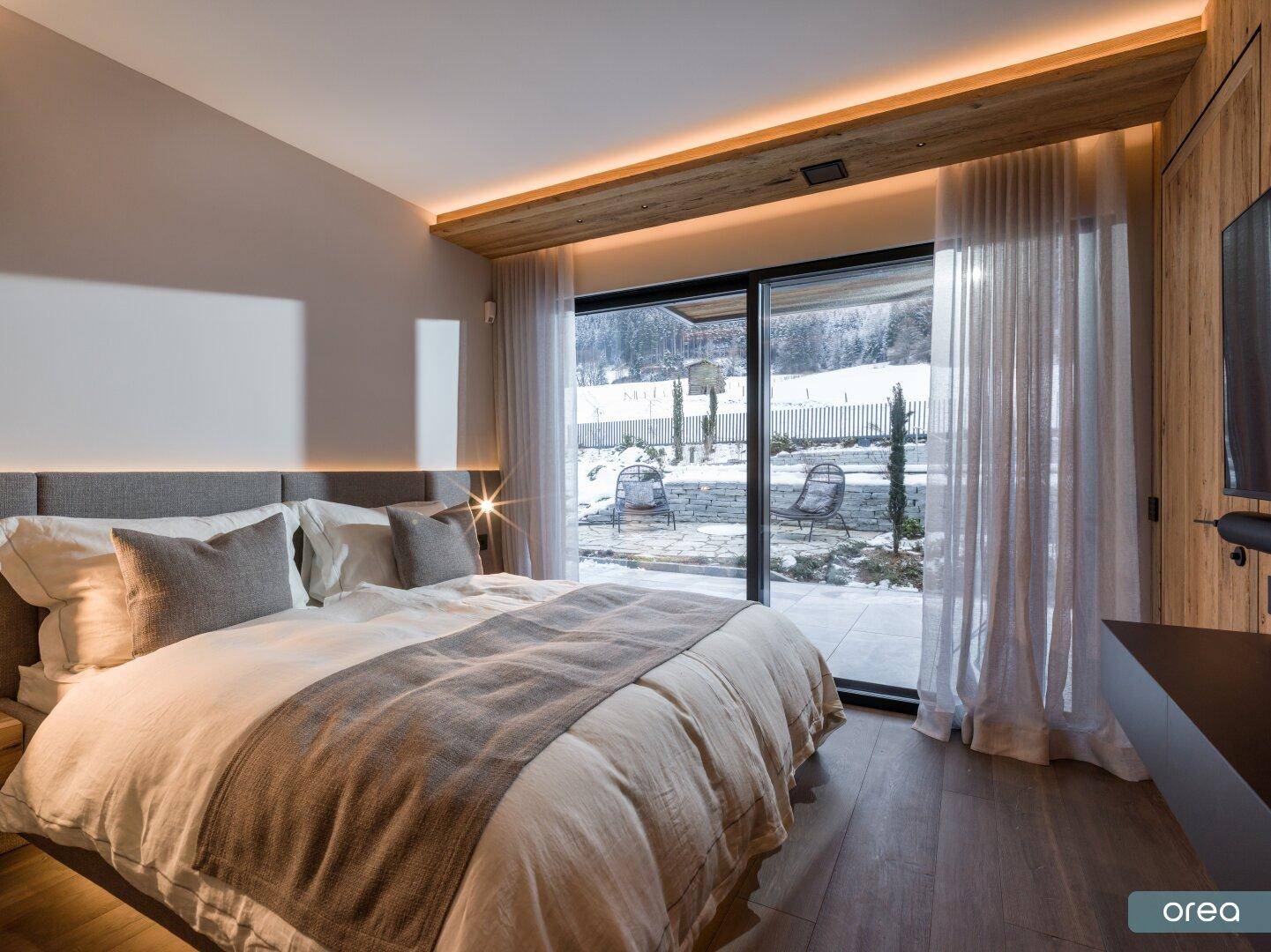 Gemütliches Schlafzimmer mit großen Schiebetüren, die den Blick auf die verschneite Landschaft freigeben.