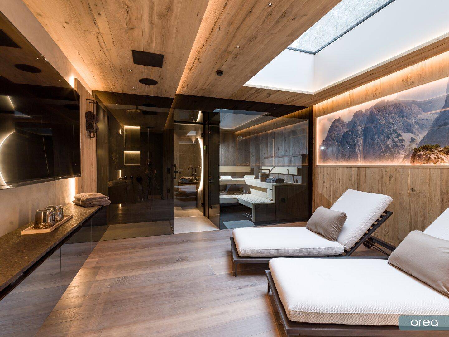 Wellnessbereich mit Sauna, Liegen und Blick auf die Berglandschaft durch ein Oberlicht.