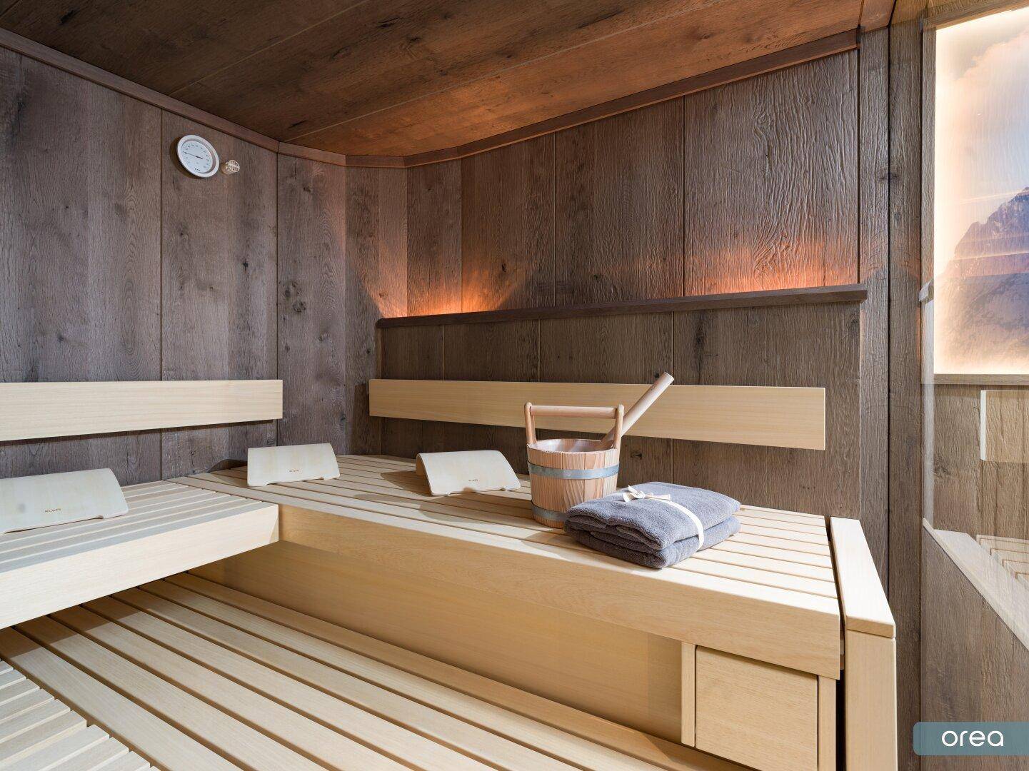 Geräumige Holzsauna mit mehreren Bänken und traditionellem Aufgusseimer.