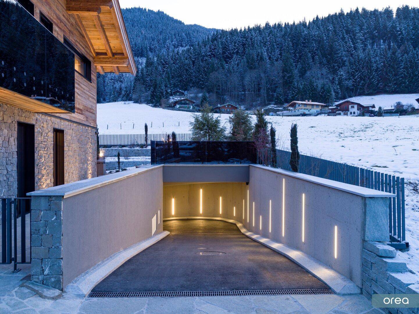 Beleuchtete Einfahrt zur Tiefgarage mit Steinmauern und moderner Beleuchtung.