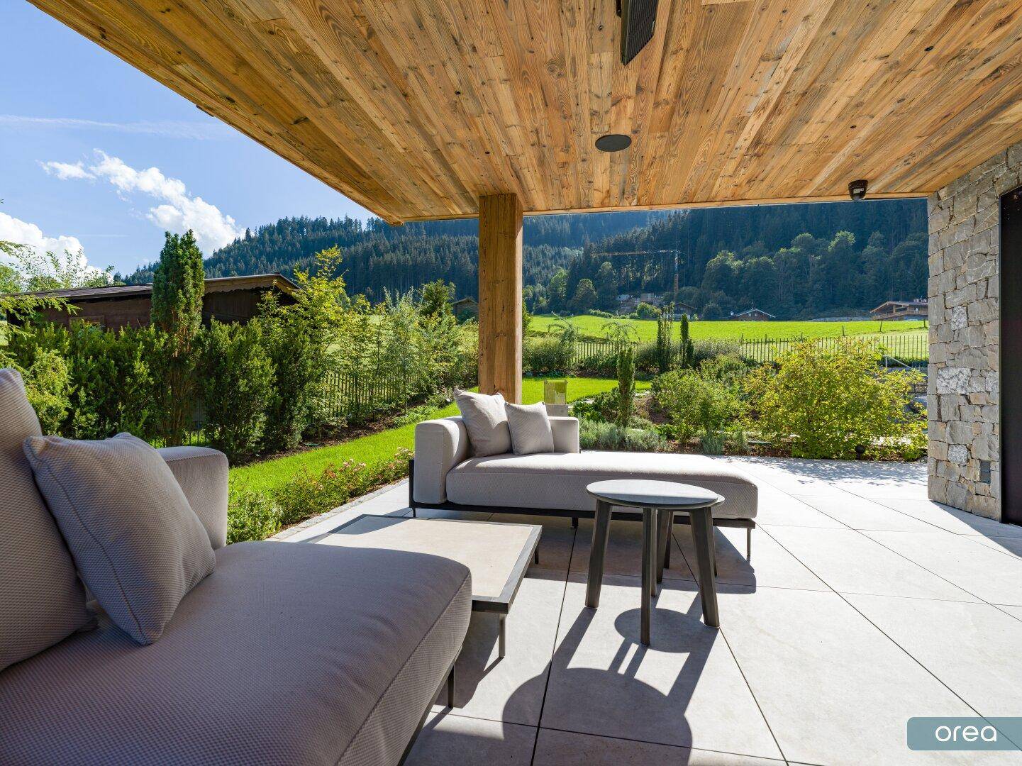 Sonnige Terrasse mit Lounge-Möbeln und Blick auf die grüne Berglandschaft im Sommer.