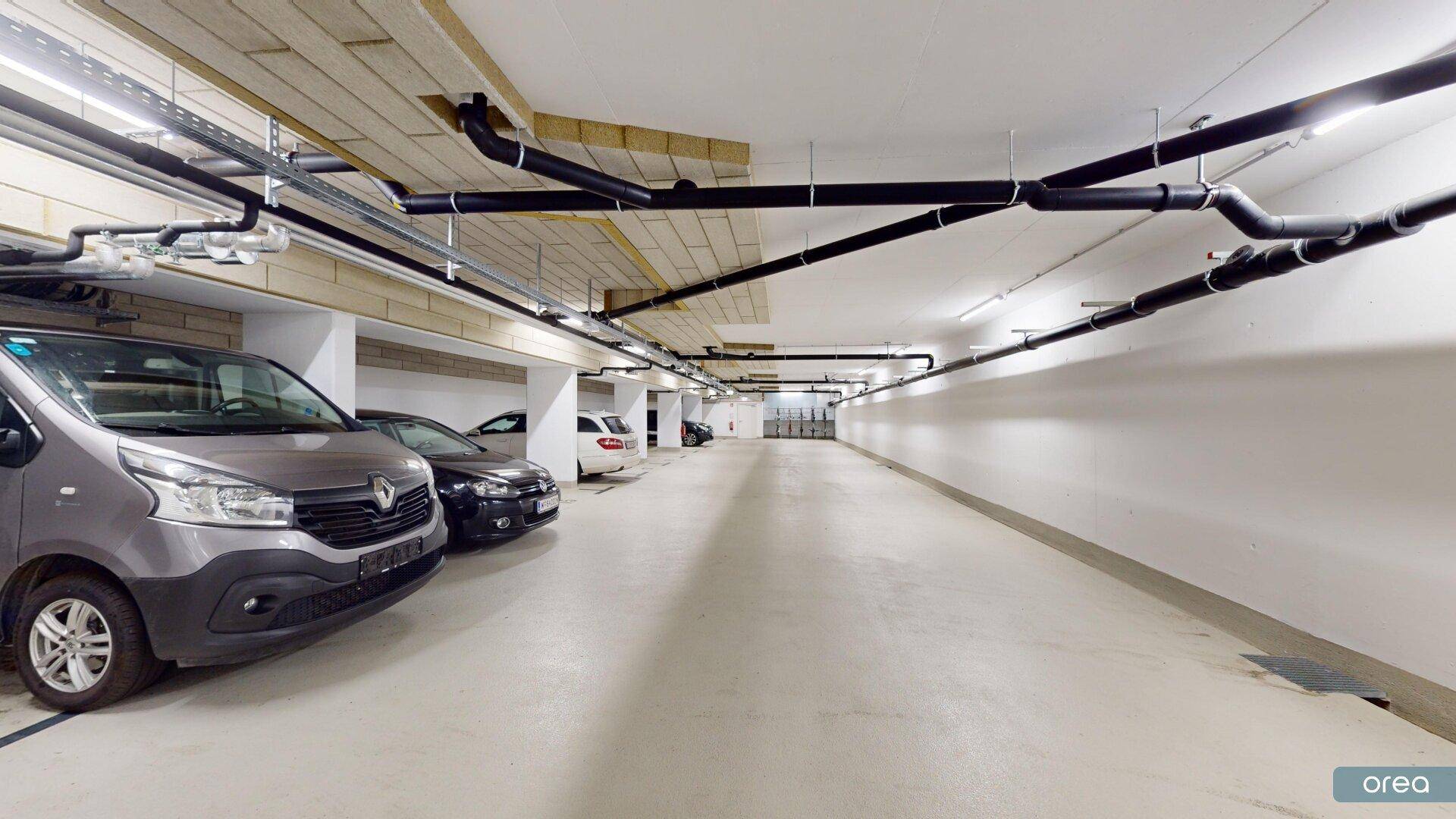 Saubere Tiefgarage mit sichtbaren Leitungen und ausreichend Parkmöglichkeiten.