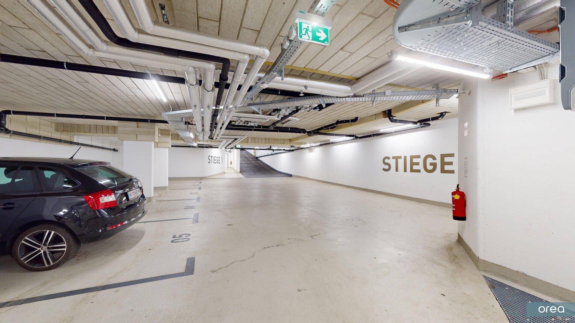 Tiefgarage mit einem geparkten Auto, sichtbaren Installationen an der Decke und einer Rampe.
