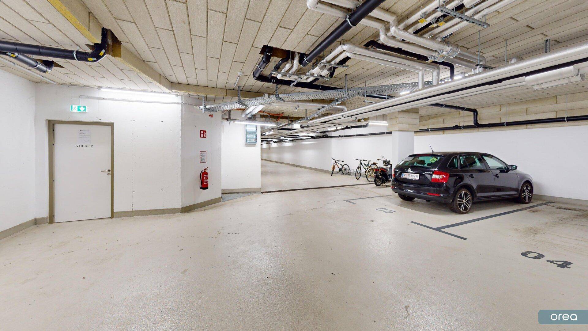 Heller Bereich einer Tiefgarage mit geparktem Auto, Fahrrädern und einer Zugangstür.