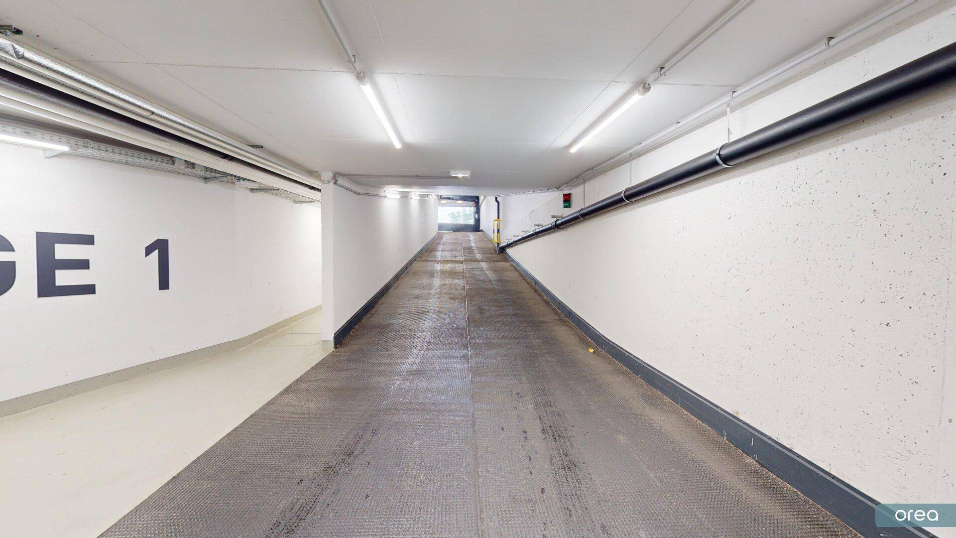 Einfahrt oder Ausfahrt einer Tiefgarage mit Rampe und heller Beleuchtung.
