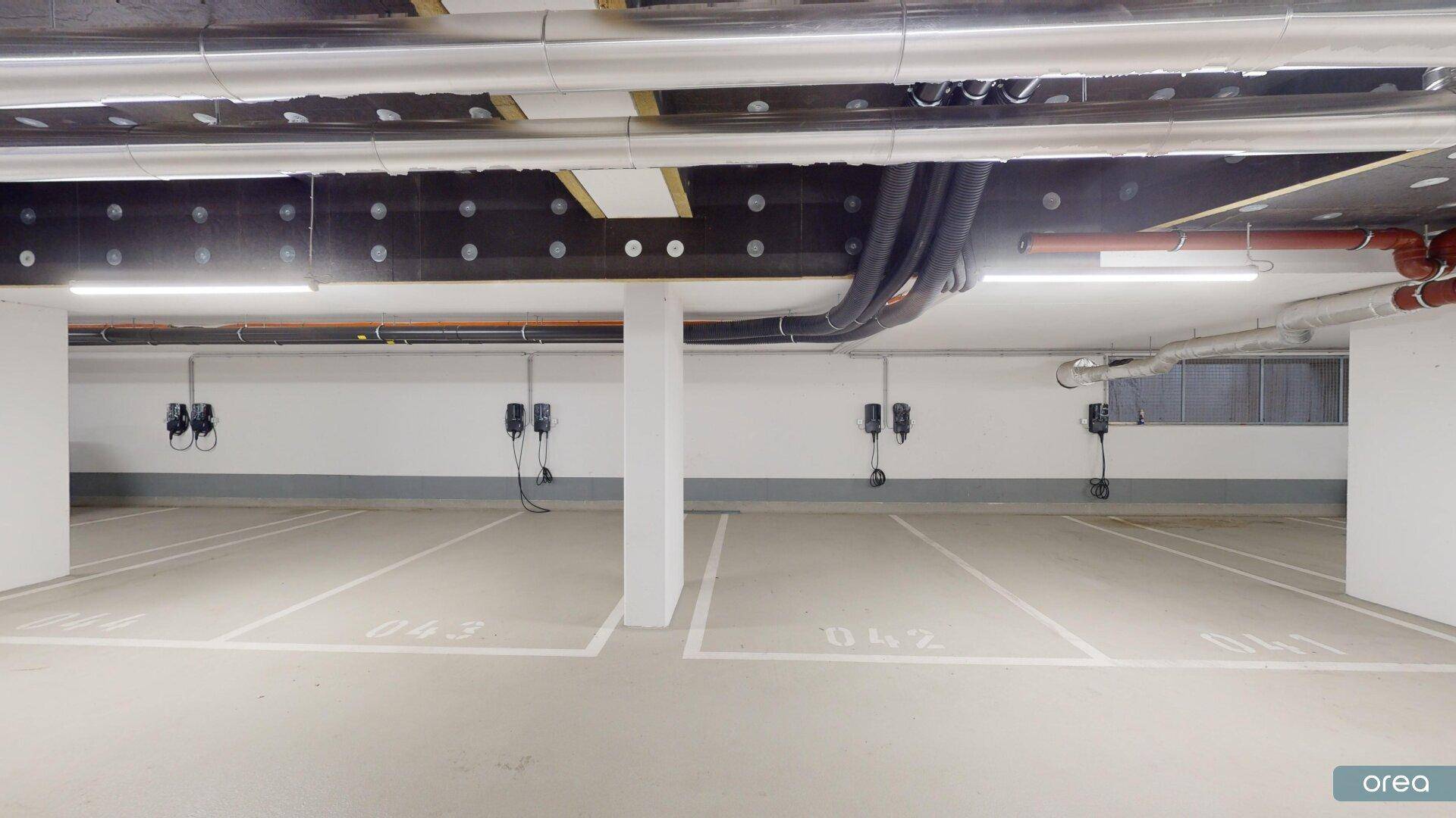 Moderne Tiefgarage mit mehreren Ladestationen für Elektrofahrzeuge an den Parkplätzen.