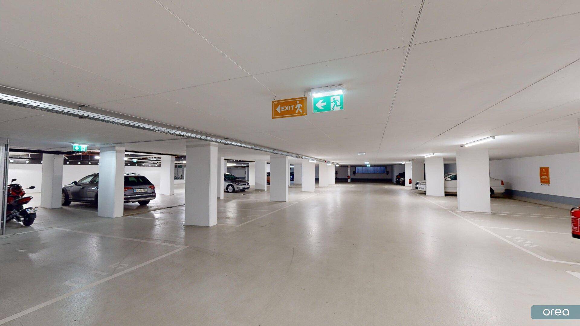 Saubere und gut beleuchtete Tiefgarage mit klarer Beschilderung für Ausgänge und Feuerlöscher.