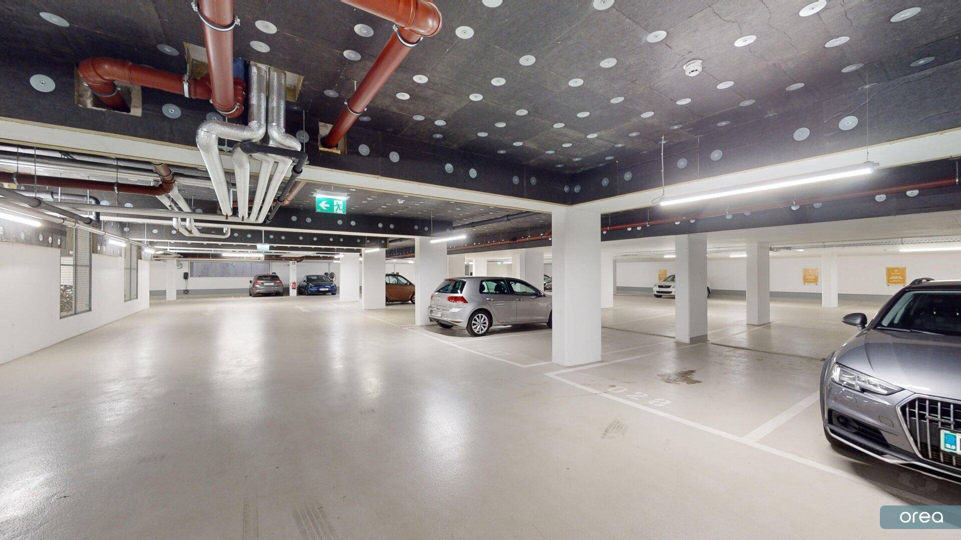 Geräumige Tiefgarage mit sichtbaren Rohrinstallationen an der Decke und modernen Fahrzeugen.