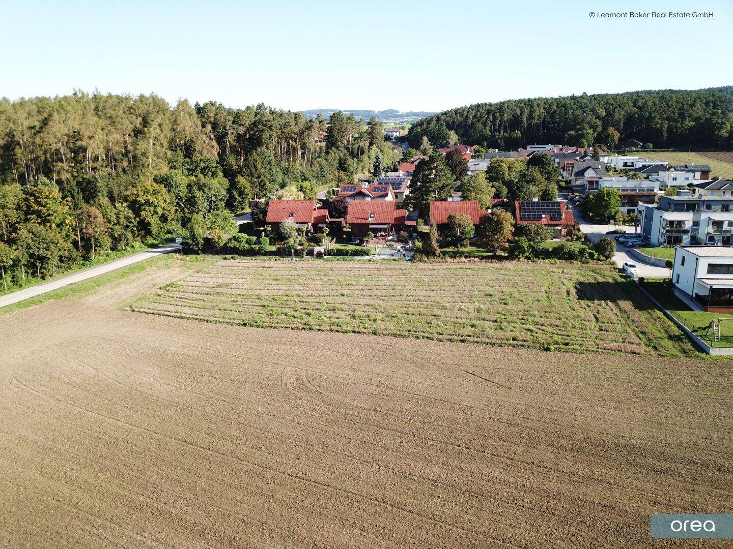 Luftaufnahme einer ländlichen Wohnsiedlung mit Feldern, Wald und verschiedenen Gebäudetypen.