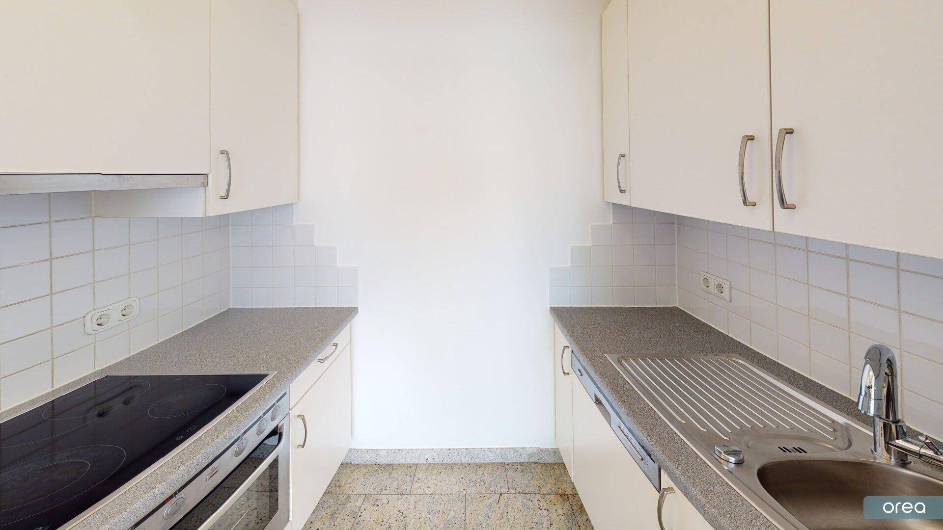 Funktionale Küche mit weißen Schränken, grauen Arbeitsplatten und einem Induktionskochfeld.
