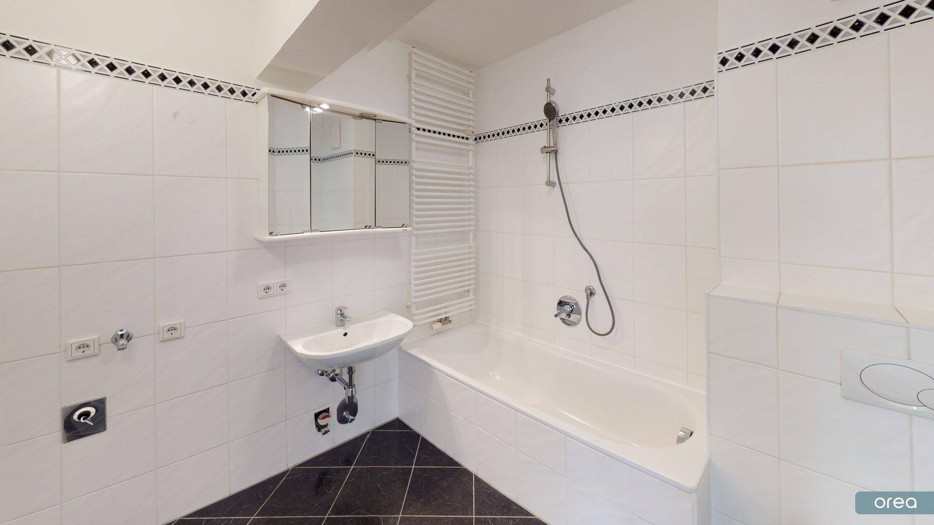 Gefliestes Badezimmer mit Badewanne, Waschbecken, Spiegelschrank und Handtuchheizkörper.