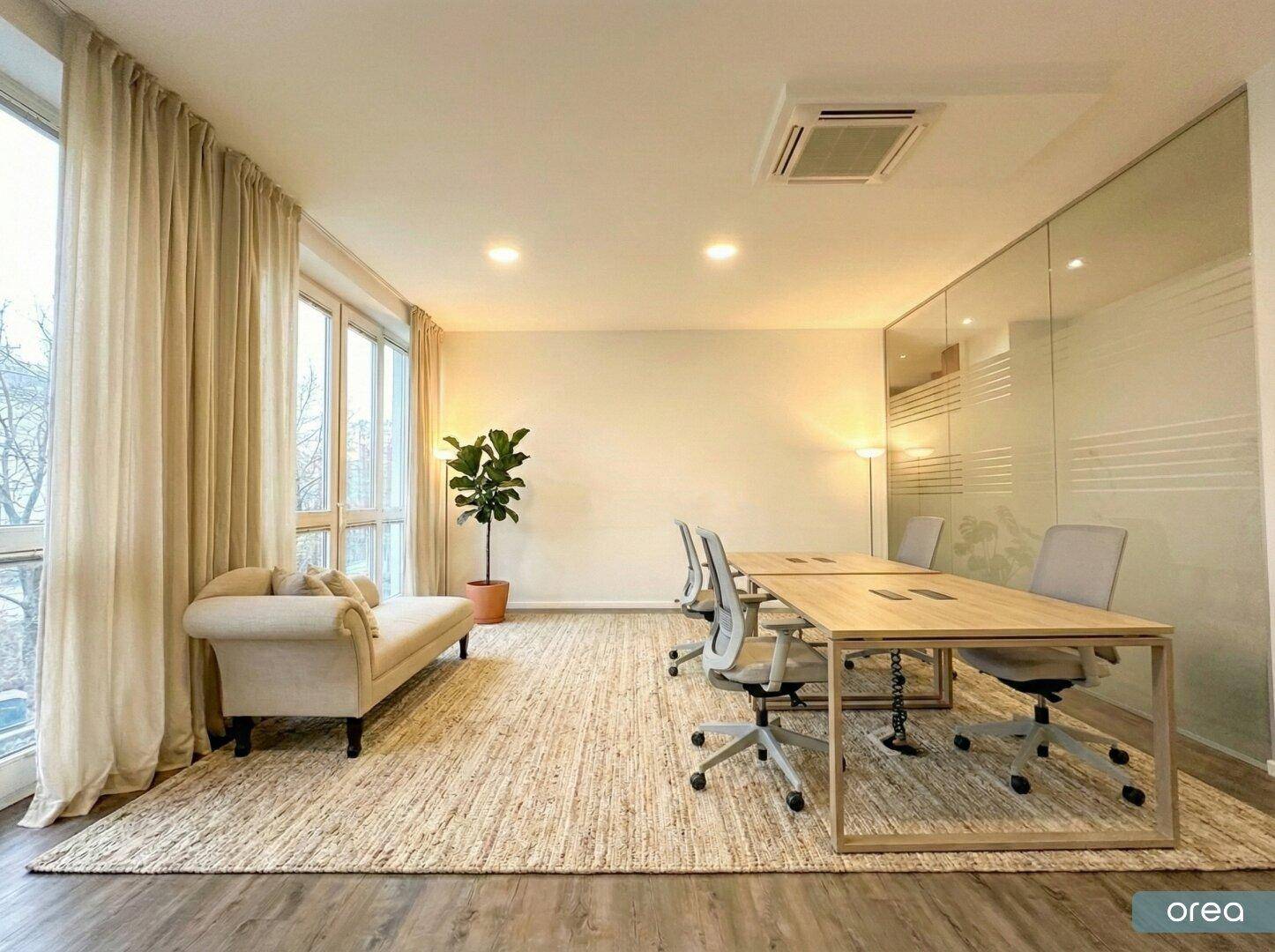 Geräumiges Büro mit Holzboden, großen Fenstern, Vorhängen und modernen Arbeitsplätzen, durch Glaswand abgetrennt.