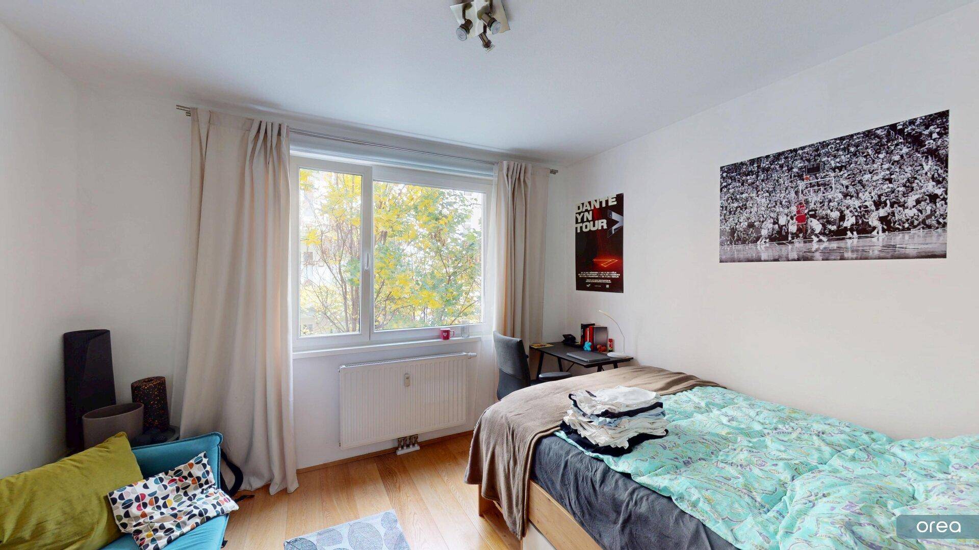 Helles Schlafzimmer mit Einzelbett, Schreibtisch und Blick ins Grüne durch das Fenster.
