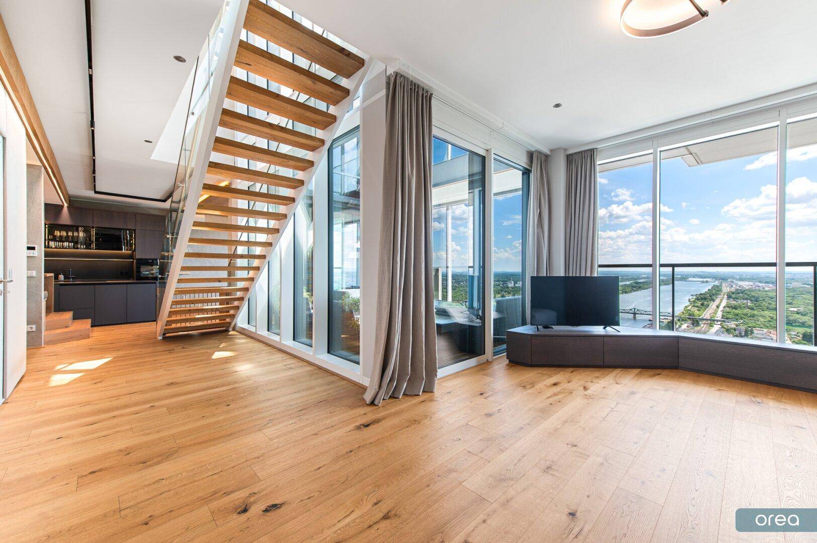 Heller Wohnbereich mit Holzparkett, moderner Treppe und Panoramablick auf den Fluss.