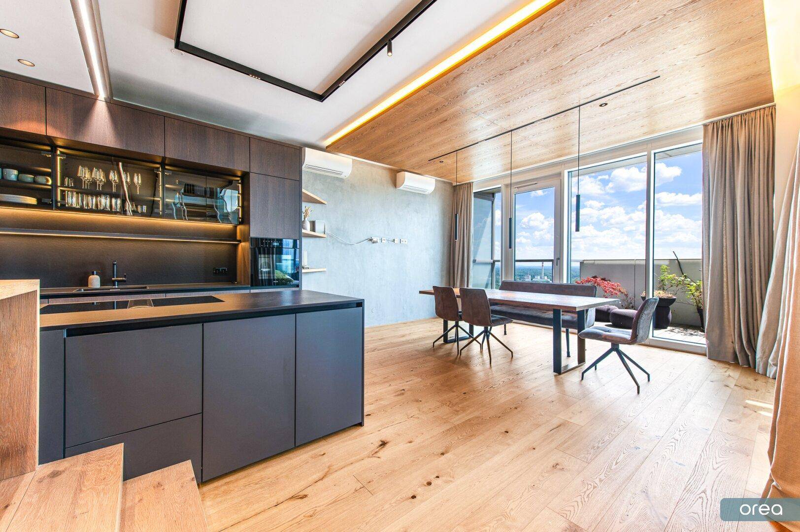 Moderne offene Küche mit dunklen Schränken, Essbereich und Zugang zur Terrasse mit Weitblick.