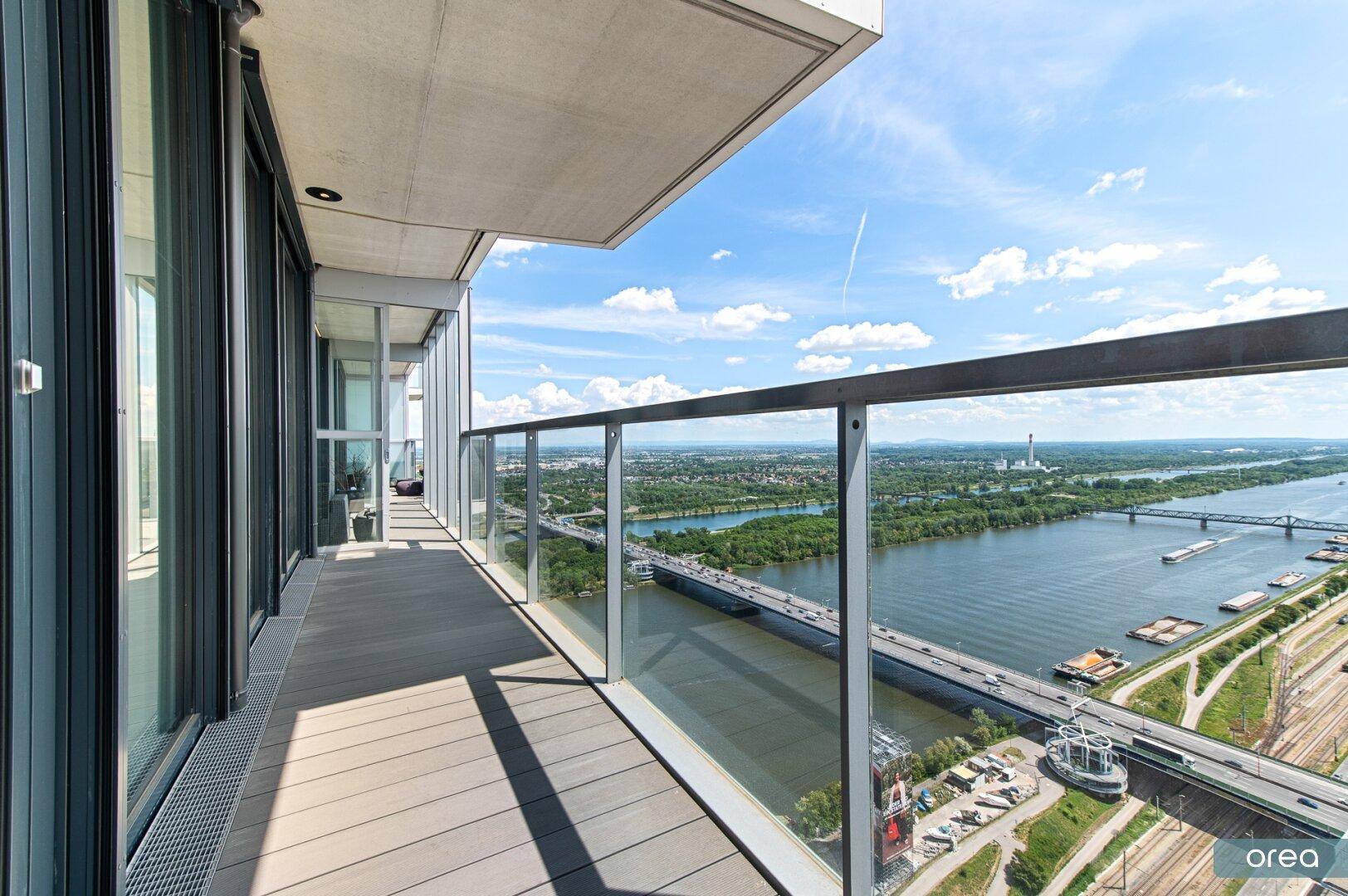 Langer Balkon mit Glasgeländer und weitem Blick auf den Fluss und die Stadtlandschaft.