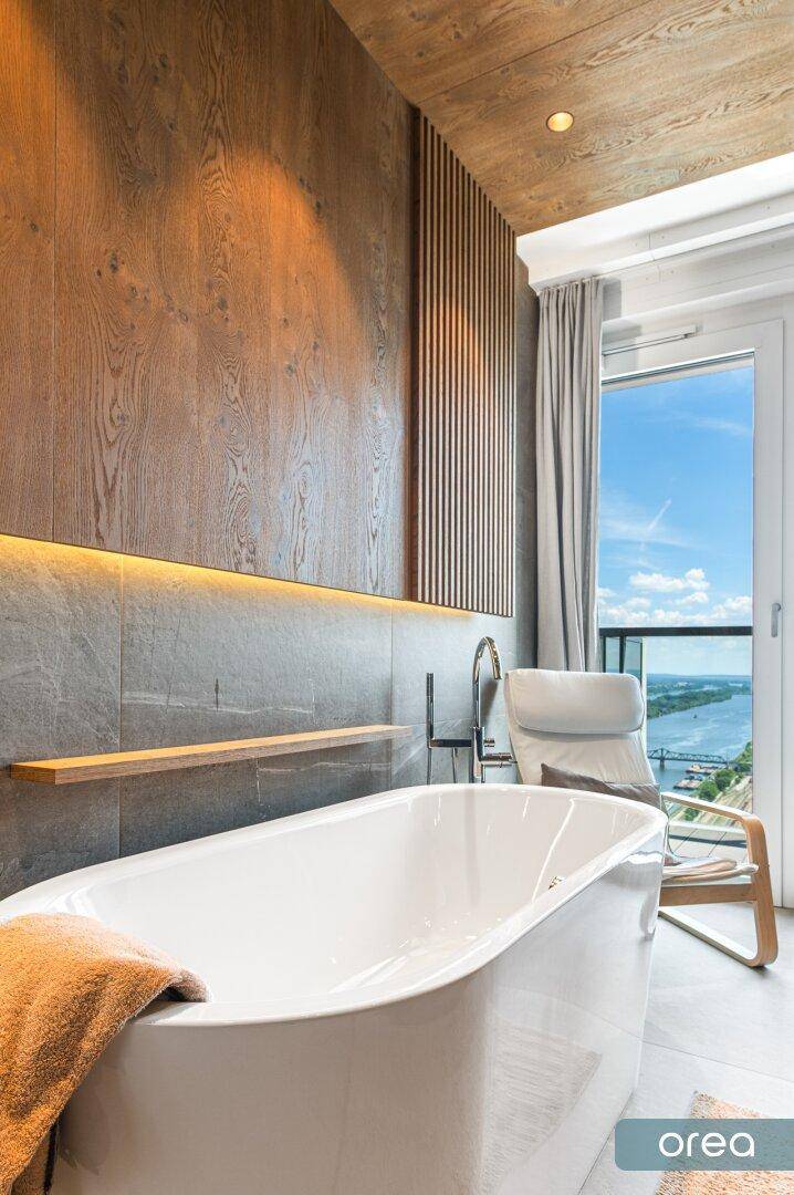 Luxuriöses Badezimmer mit freistehender Badewanne, Holzverkleidung und Blick ins Grüne.