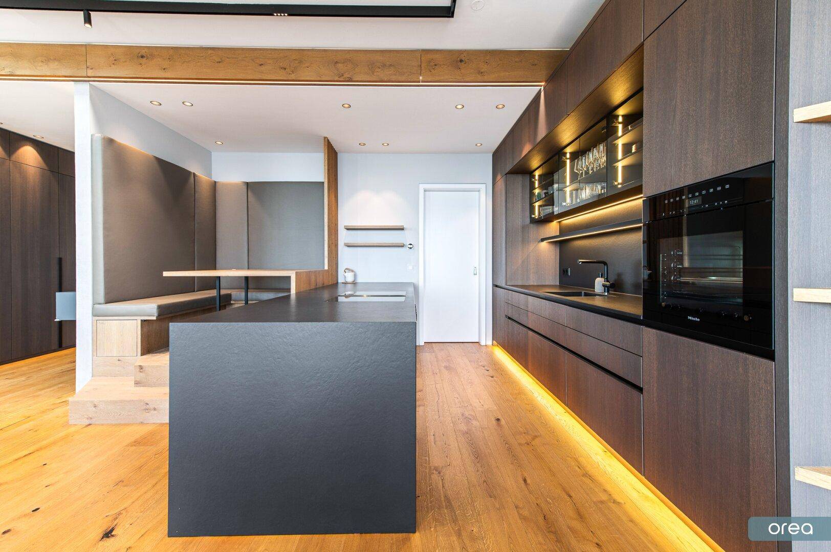 Elegante Küche mit dunklen Holzfronten, Kochinsel und integriertem Essbereich mit Sitzbank.