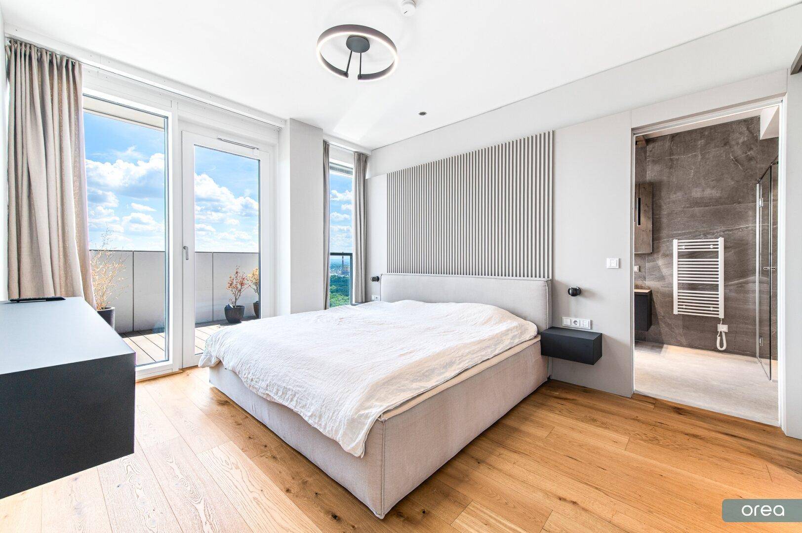 Modernes Schlafzimmer mit Holzboden, Zugang zum Balkon und angrenzendem Badezimmer.