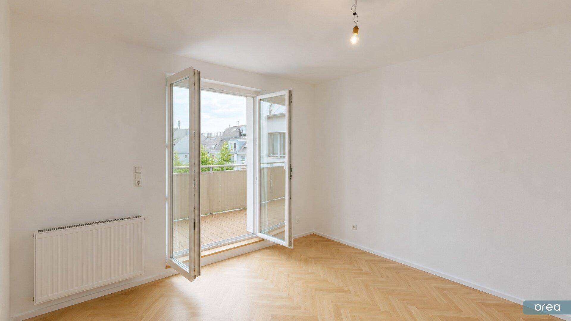 Heller Wohnraum mit Fischgrätparkett und Zugang zu einem Balkon.