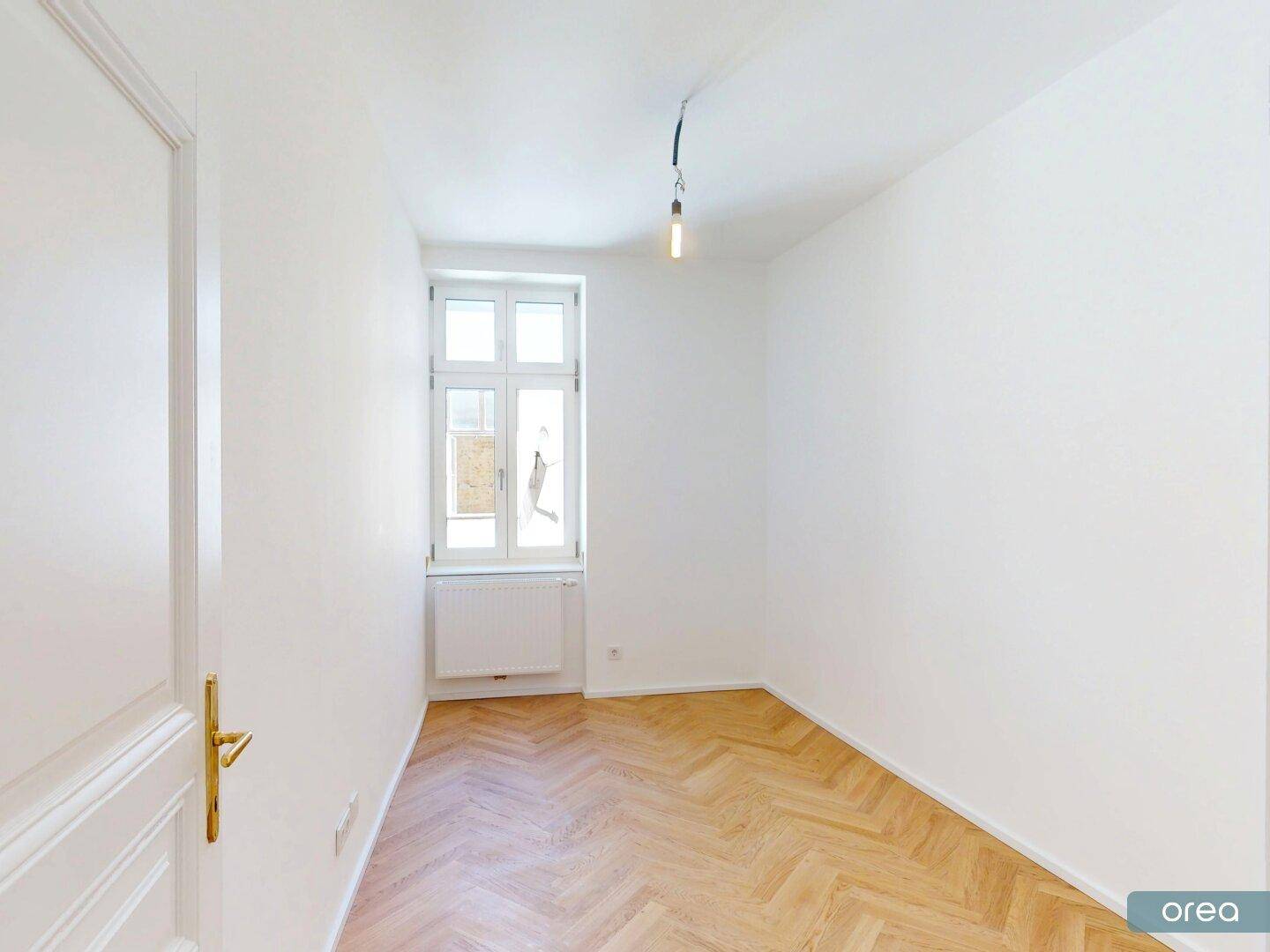 Ruhiges Zimmer mit einem Fenster, Fischgrätparkett und frisch gestrichenen weißen Wänden.