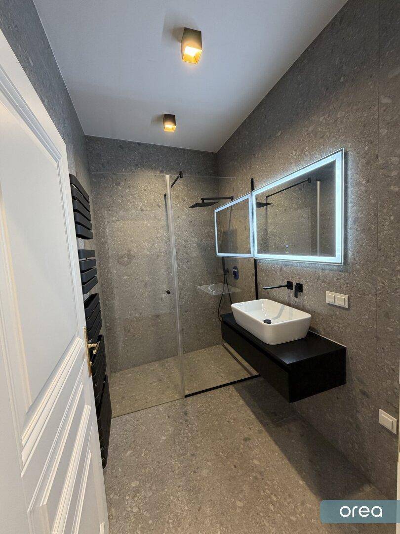 Modernes Badezimmer mit begehbarer Dusche, schwebendem Waschtisch und grauen Fliesen im Terrazzo-Stil.