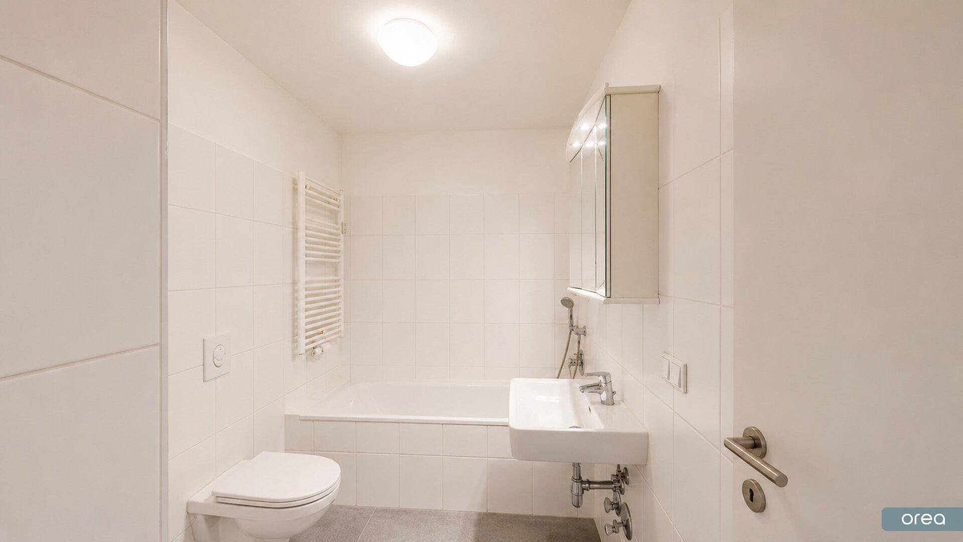 Helles Badezimmer mit Badewanne, WC, Waschbecken und einem beheizten Handtuchhalter.