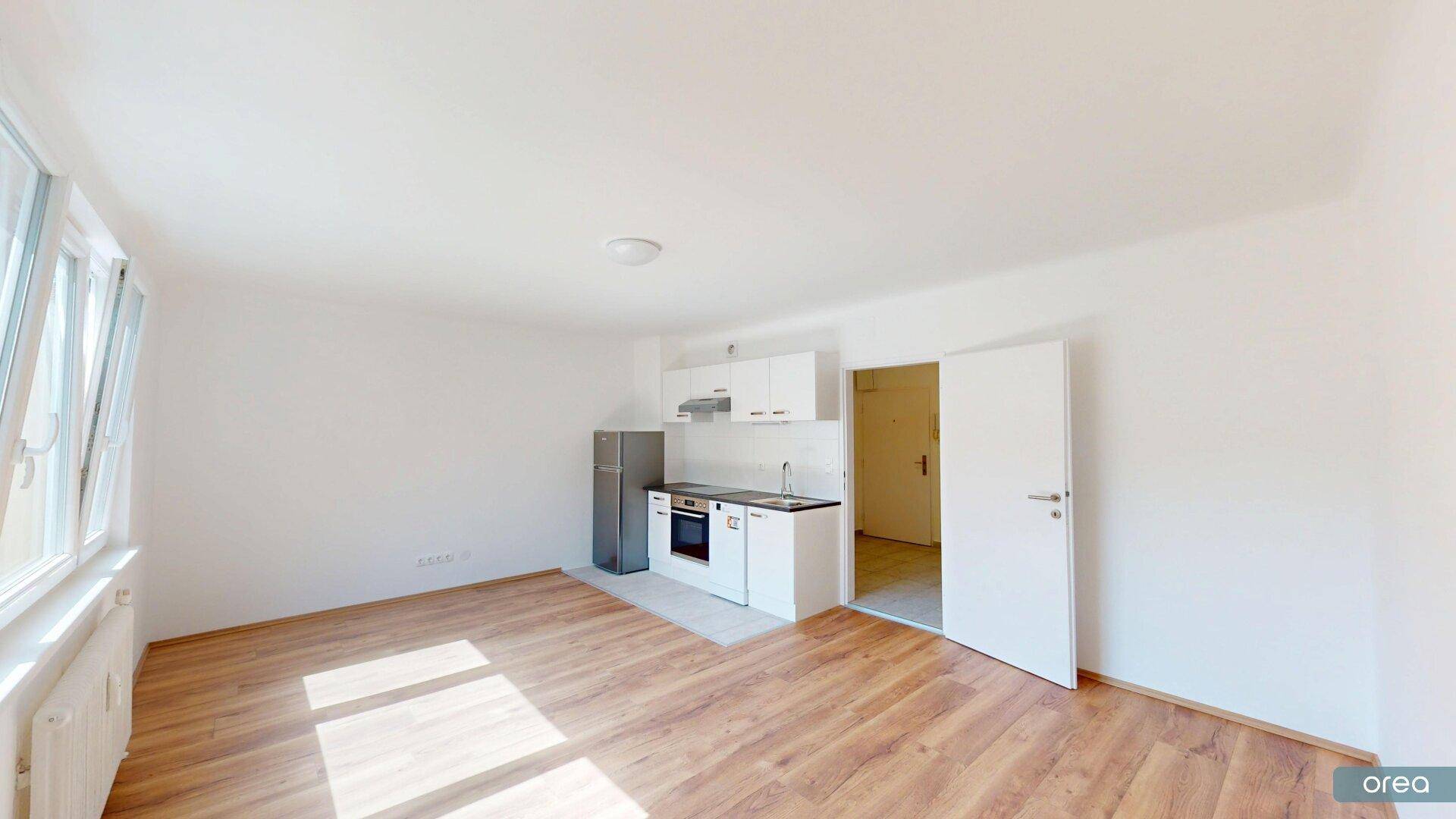 Geräumiger Wohnbereich mit integrierter Küchenzeile und Zugang zu einem weiteren Raum, ideal für ein Studio-Apartment.