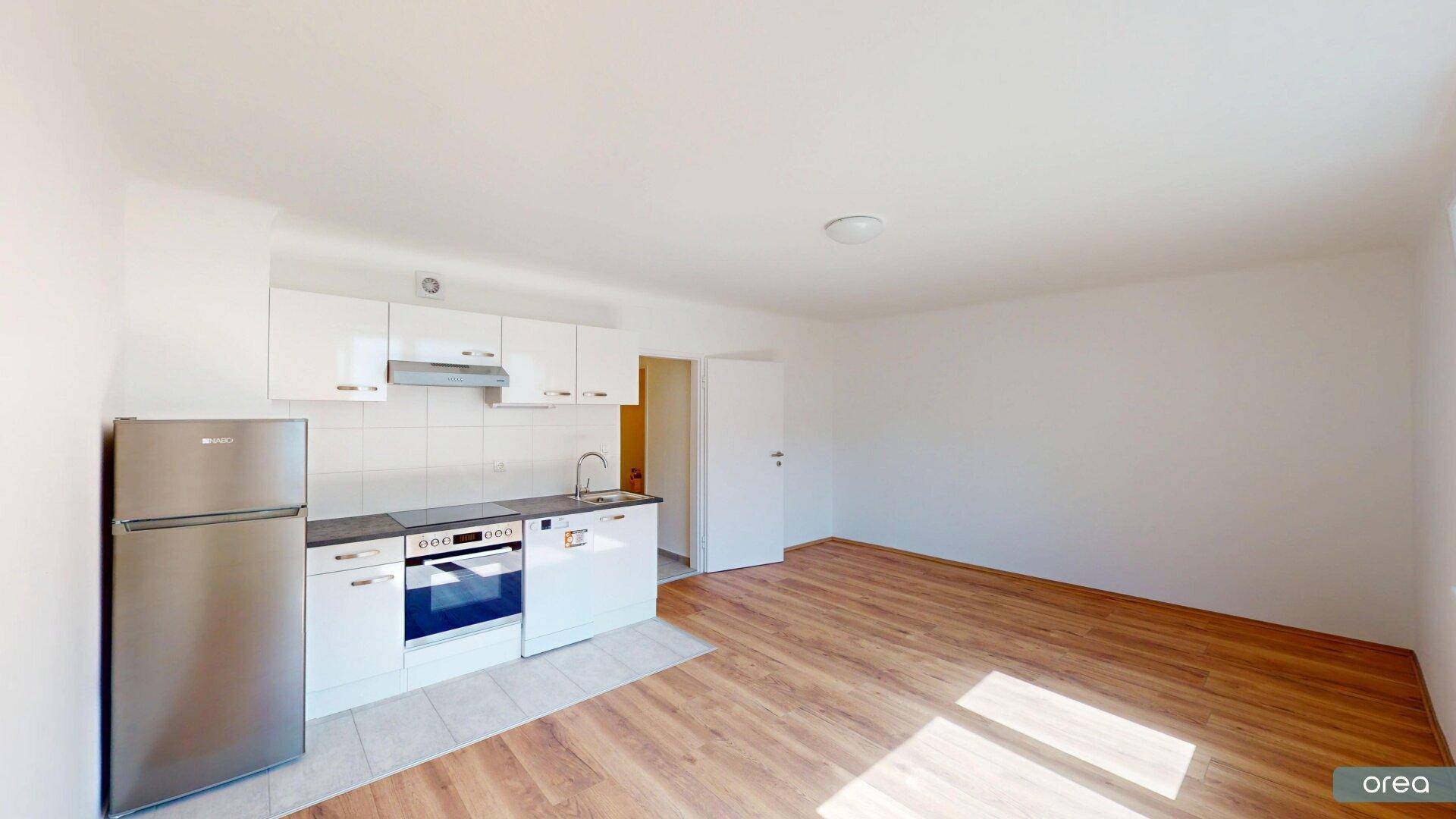 Moderne Küchenzeile mit weißen Hochglanzschränken, integriertem Backofen und Kühlschrank in einem offenen Wohnbereich.