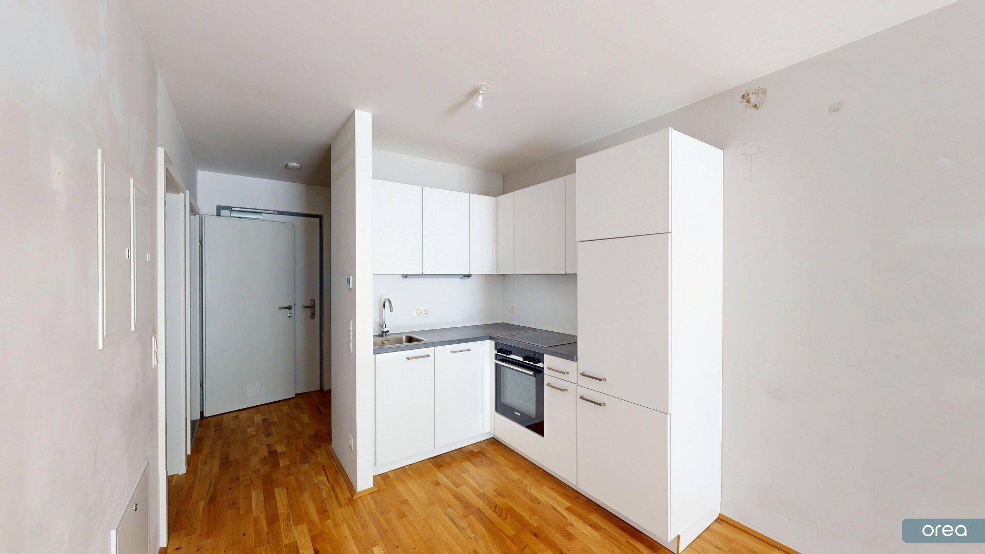 Moderne Küchenzeile mit weißen Schränken und integriertem Backofen in einem hellen Raum mit Holzboden.