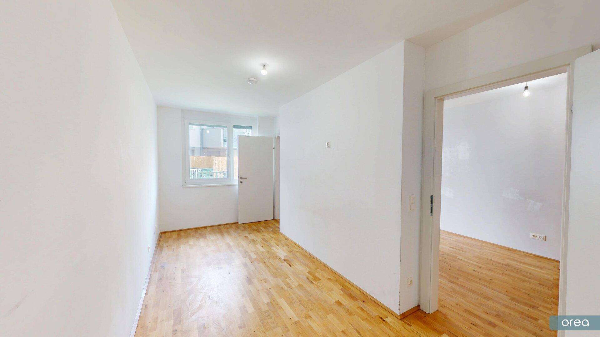Helles Schlafzimmer mit Holzboden und einem Fenster, das Tageslicht hereinlässt.