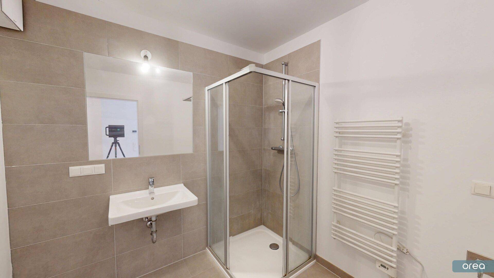 Modernes Badezimmer mit beigefarbenen Fliesen, Duschkabine und beheiztem Handtuchhalter.