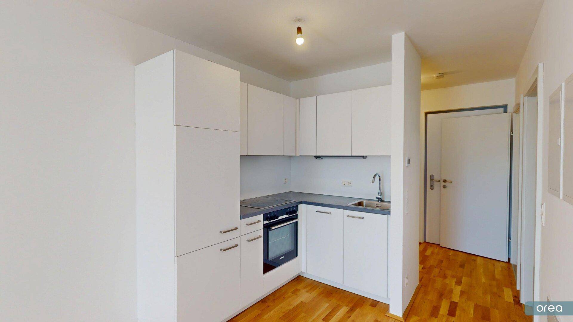 Moderne, kompakte Küchenzeile mit weißen Schränken, integriertem Backofen und Spüle.