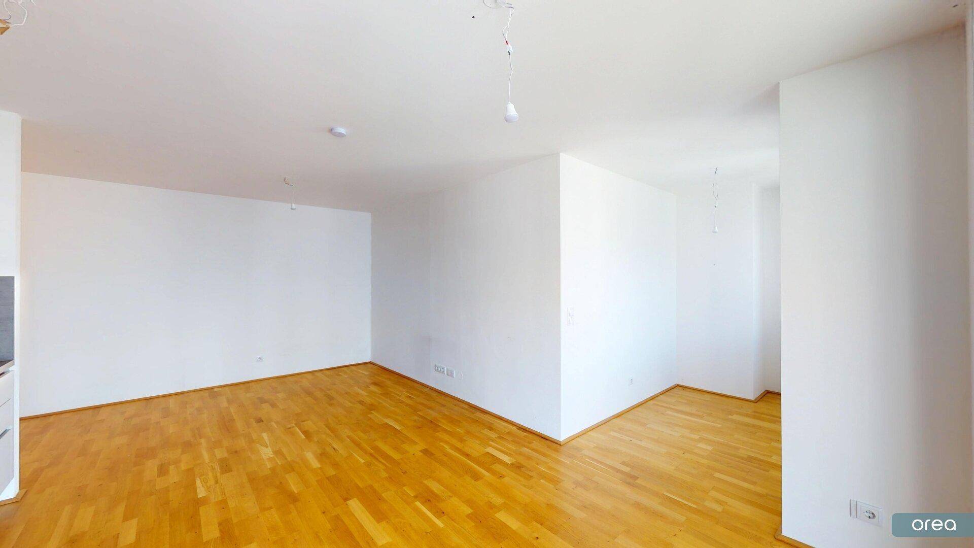Geräumiger, heller Wohnbereich mit Holzboden und weißen Wänden, bereit zur Einrichtung.