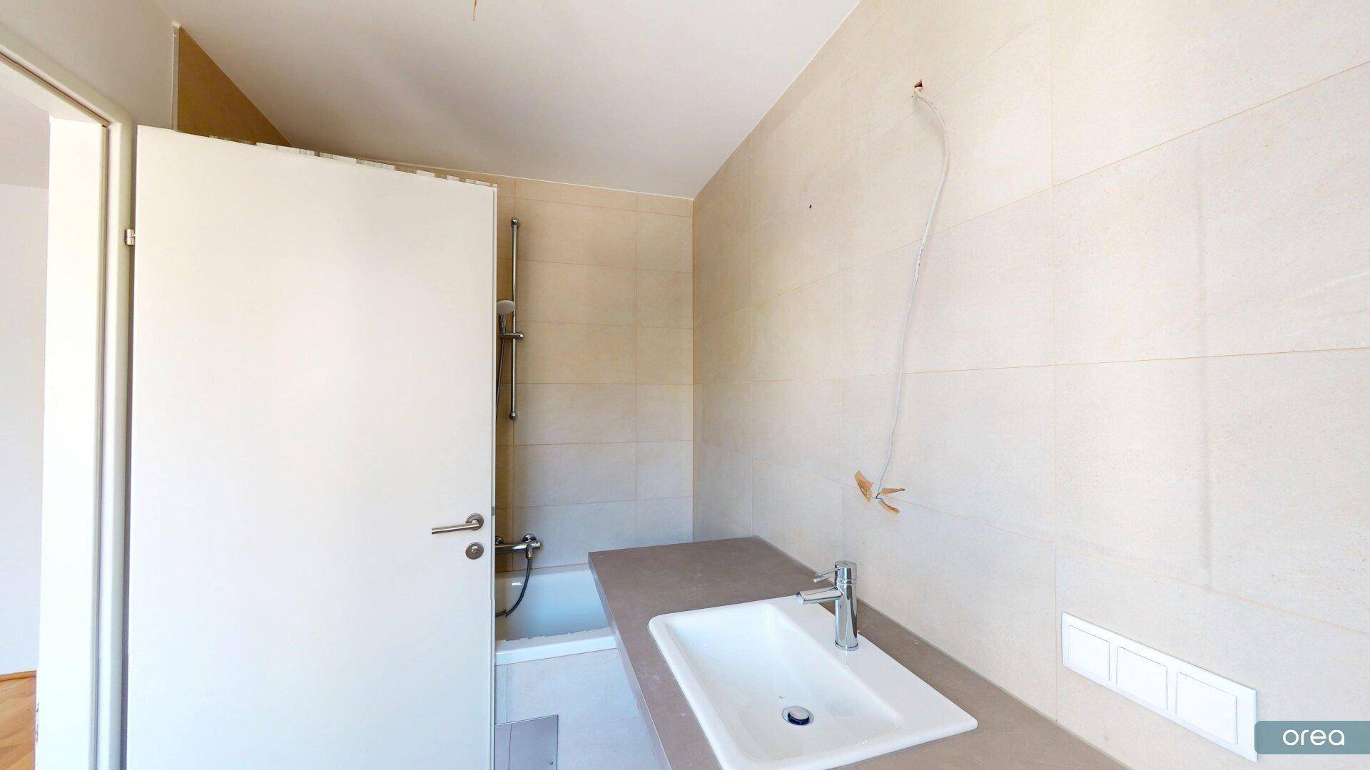 Modernes Badezimmer mit hellen Fliesen, Waschtisch und Badewanne mit Duschfunktion.