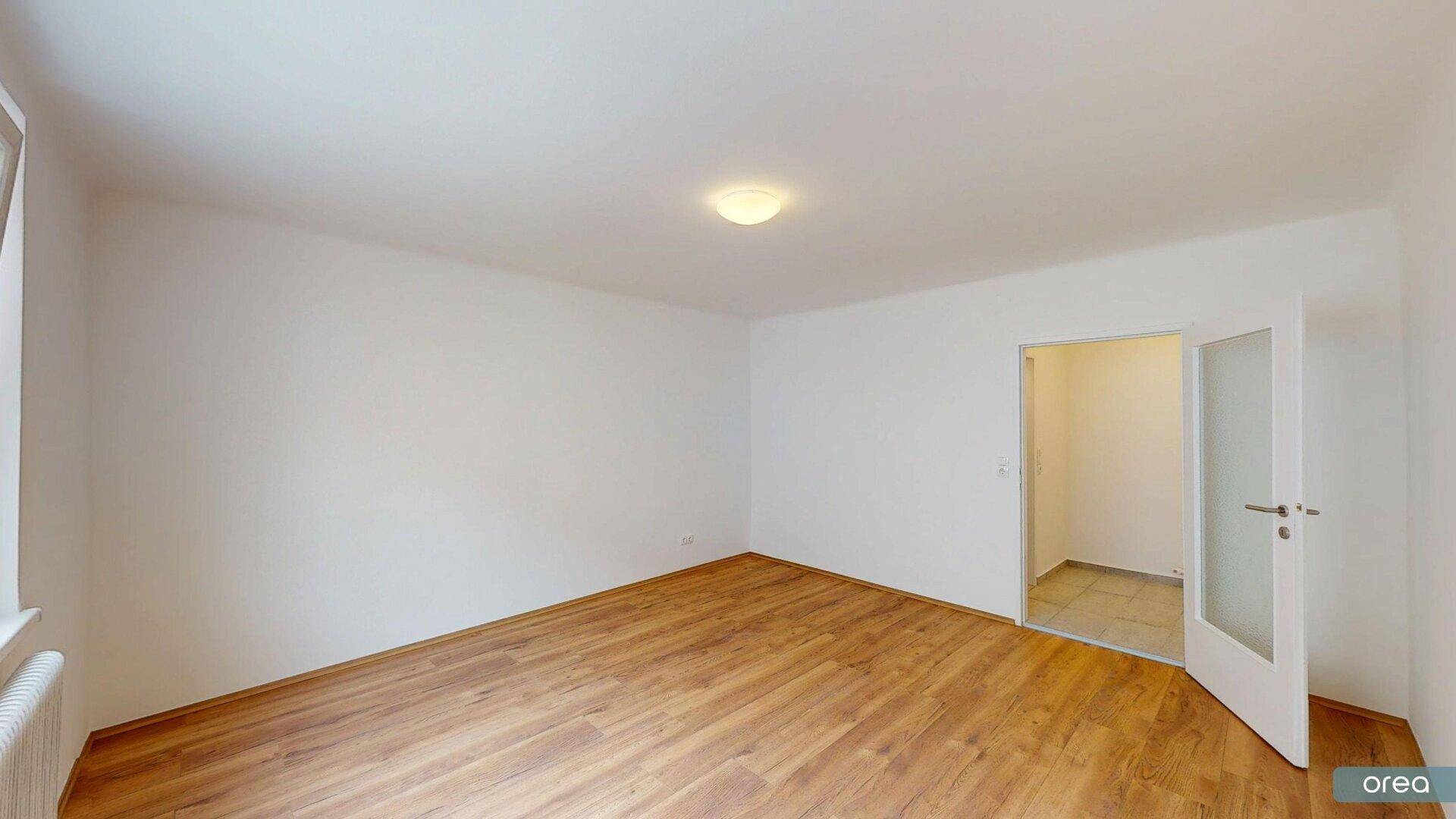 Geräumiges Zimmer mit Laminatboden und einer Tür, die zu einem weiteren Bereich führt.