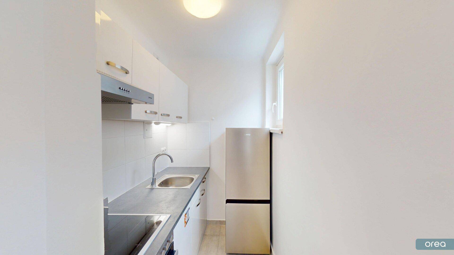Kleine, funktionale Küche mit weißen Schränken, Spüle und einem freistehenden Kühlschrank.