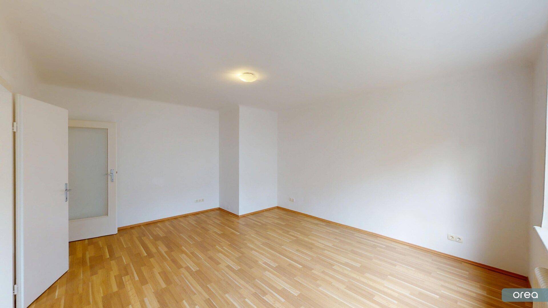 Geräumiges, leeres Zimmer mit hellem Holzfußboden und weiß gestrichenen Wänden.