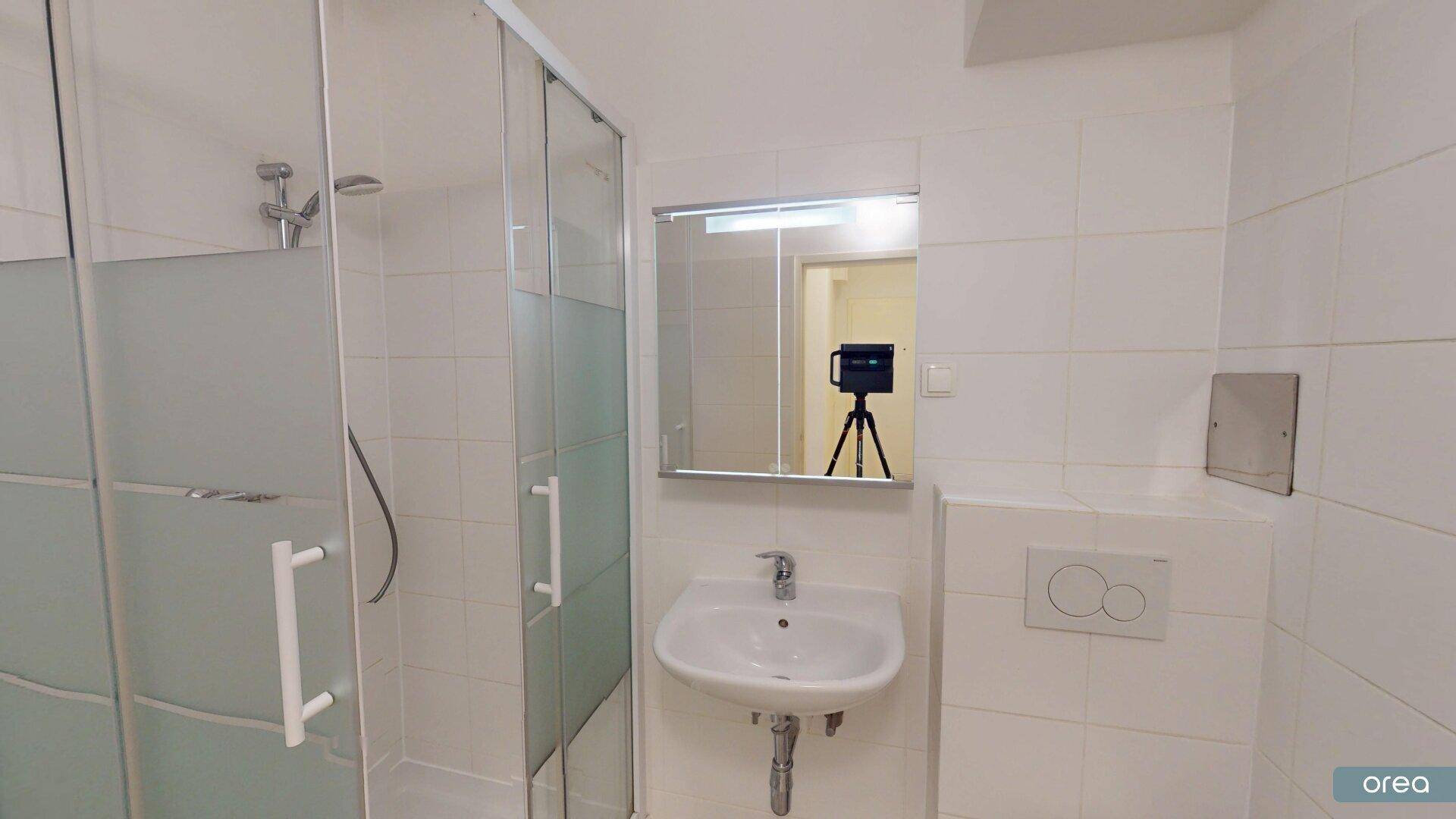 Modernes Badezimmer mit Duschkabine, Waschbecken und wandhängendem WC, komplett gefliest.
