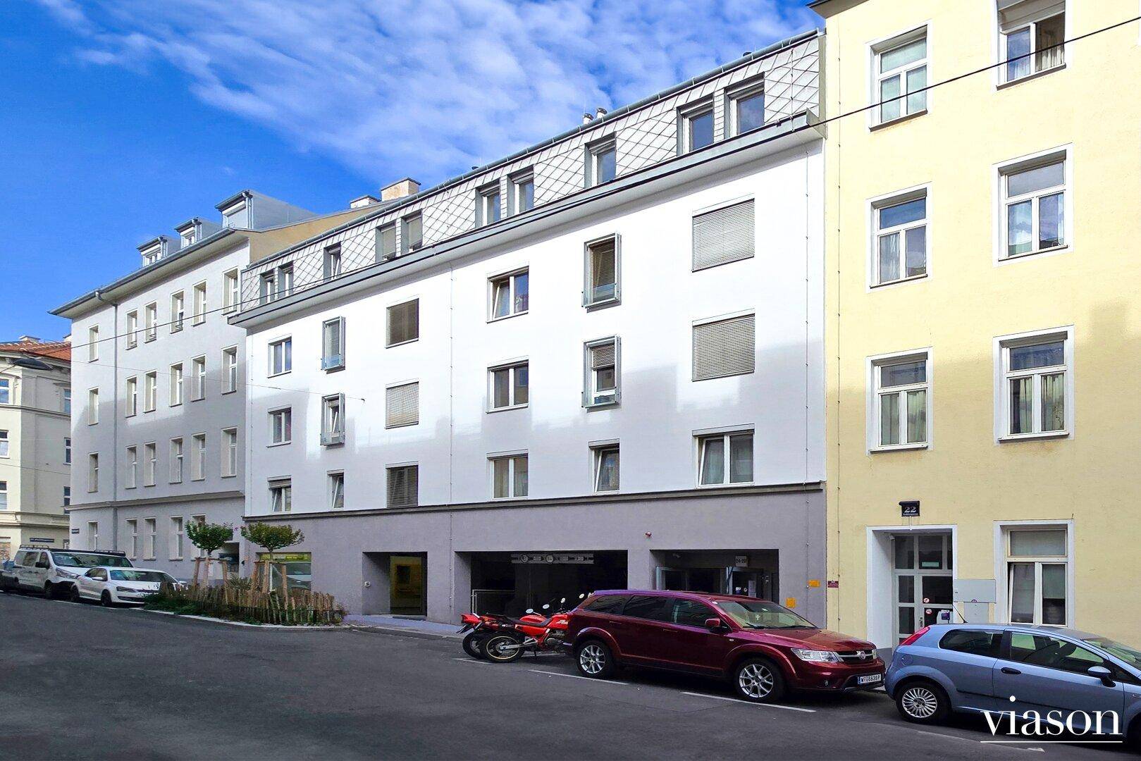 Mehrstöckiges Wohngebäude mit moderner Fassade und Parkplätzen an der Straße.