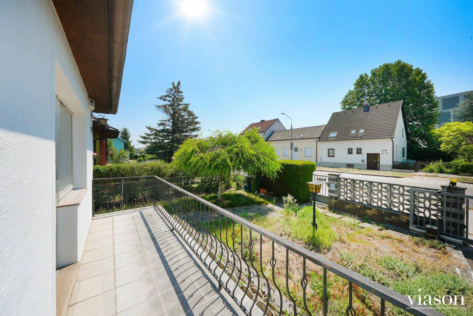 Sonniger Balkon mit schmiedeeisernem Geländer und Blick auf den Vorgarten.