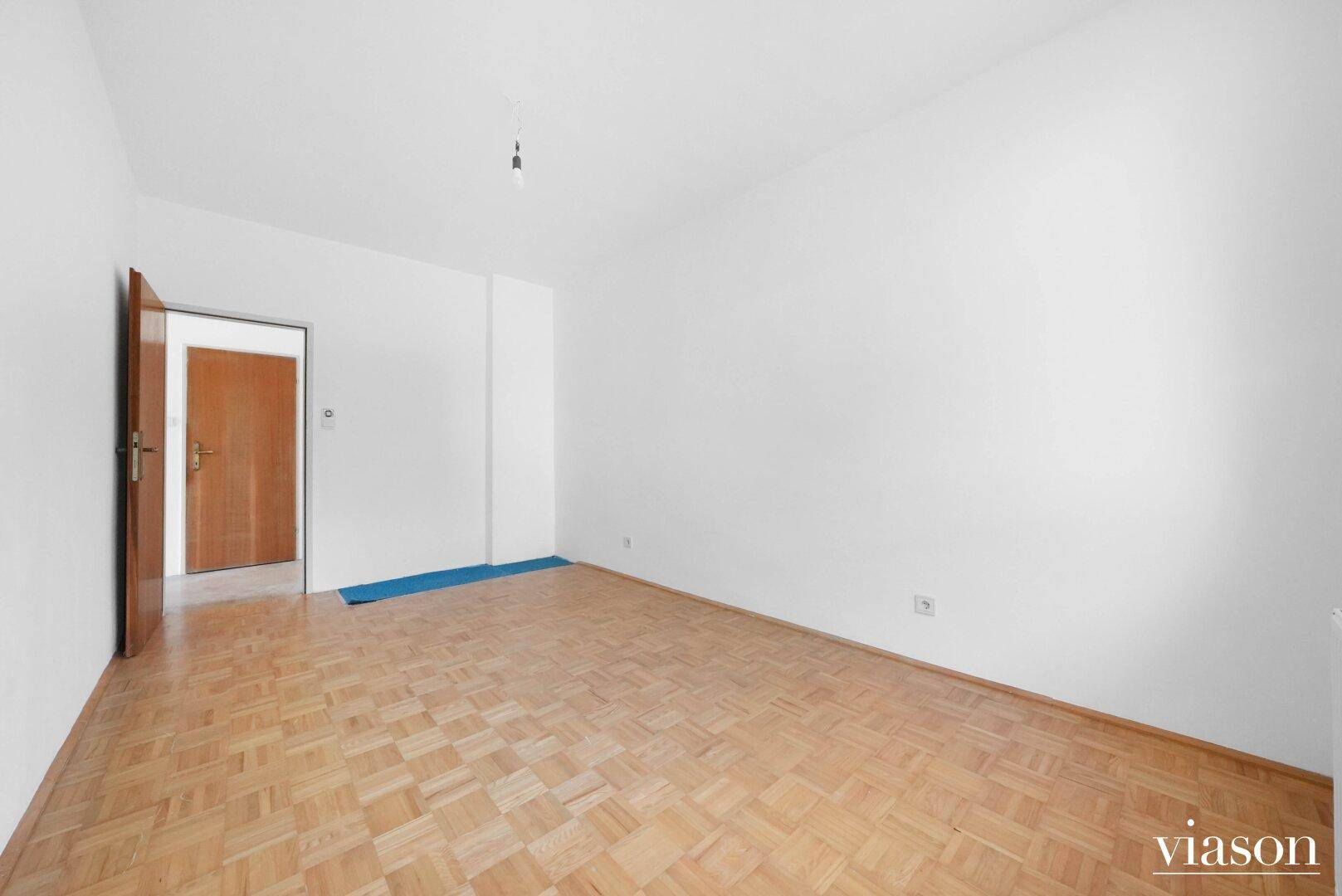 Helles Schlafzimmer mit Parkettboden und einfacher Ausstattung.