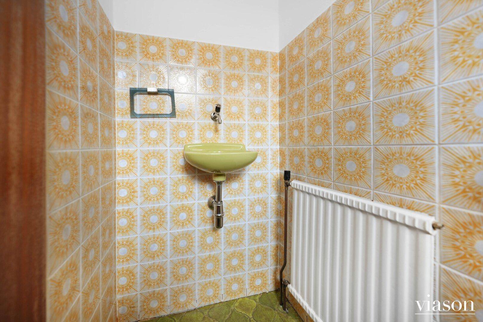 Kleines WC mit gelbem Waschbecken und gemusterten Fliesen, passend zum Retro-Design.