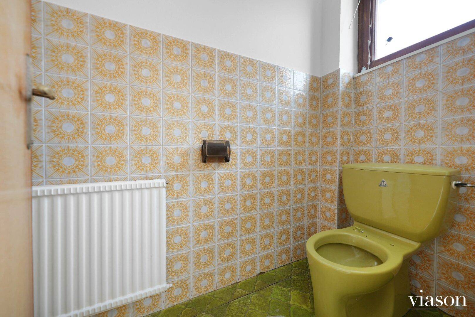 Separate Toilette mit gelber Keramik und auffälligen gelb-weißen Fliesen im Retro-Stil.