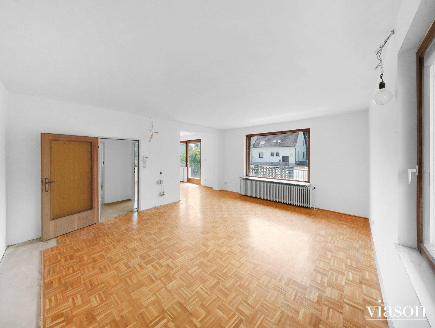 Geräumiges Wohnzimmer mit Parkettboden, Heizkörper und Blick auf die Umgebung.