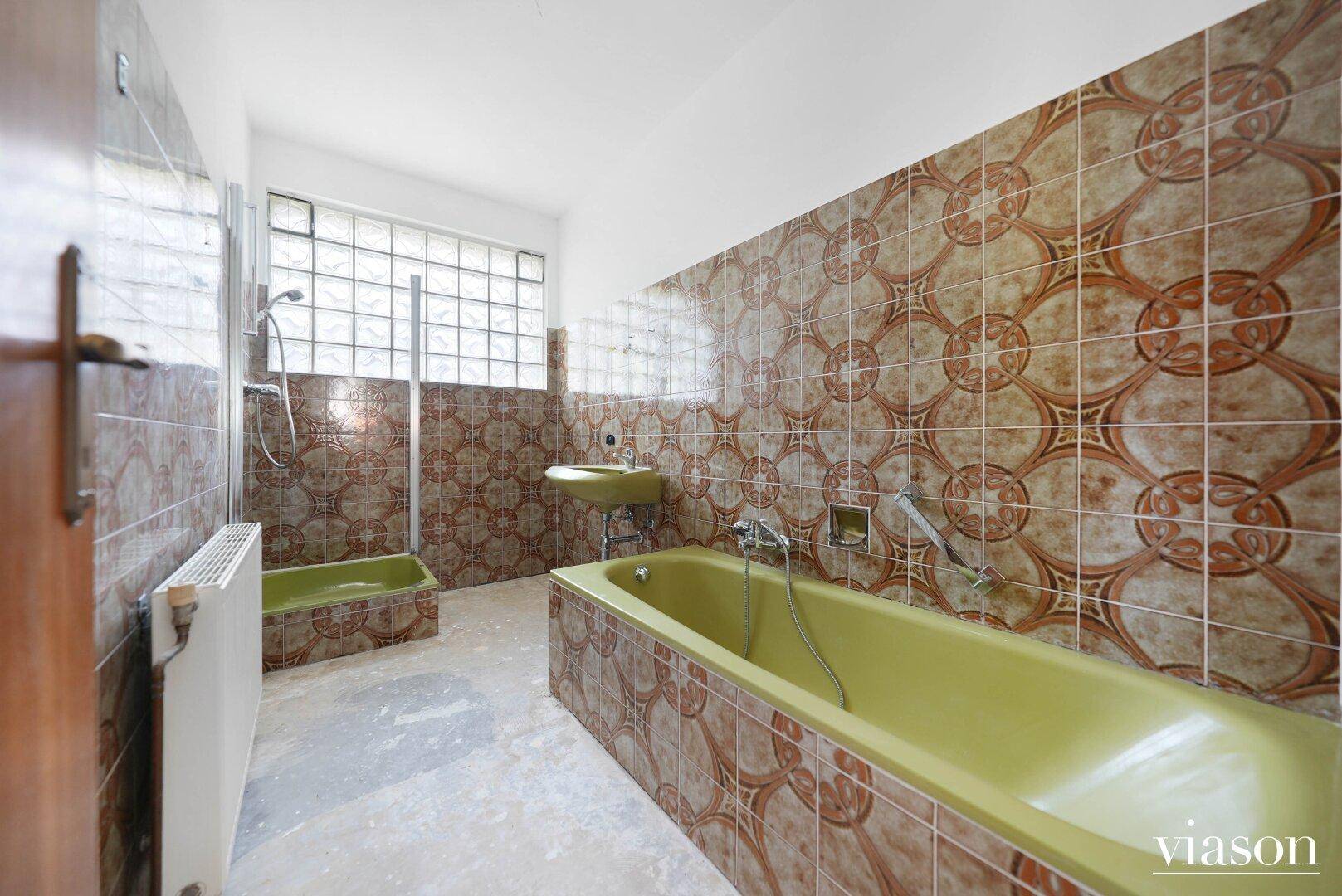 Badezimmer im Stil der 80er Jahre mit grüner Badewanne, Dusche und gemusterten Fliesen.