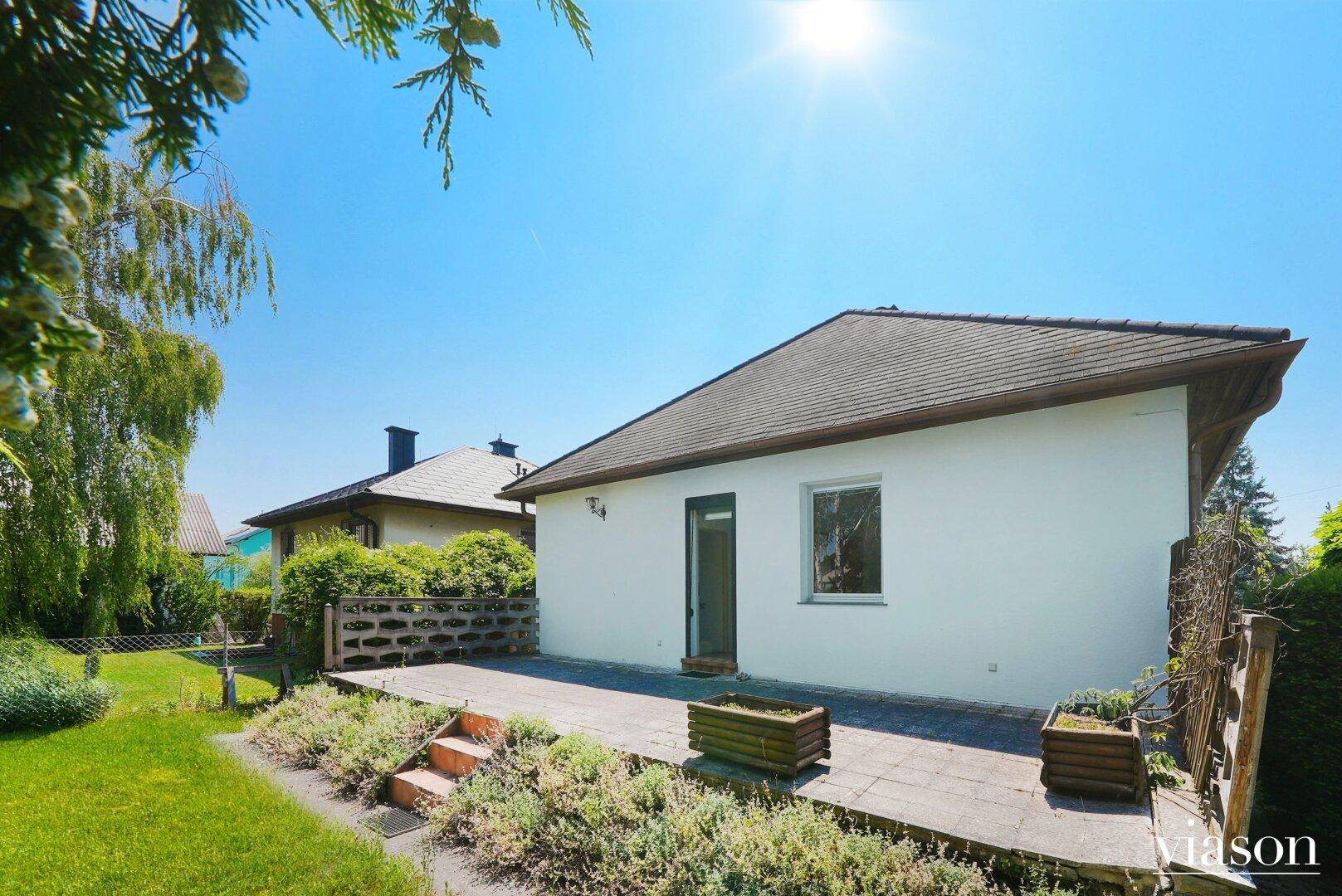 Rückseite des Hauses mit Holzterrasse und Zugang zum weitläufigen, sonnigen Garten.