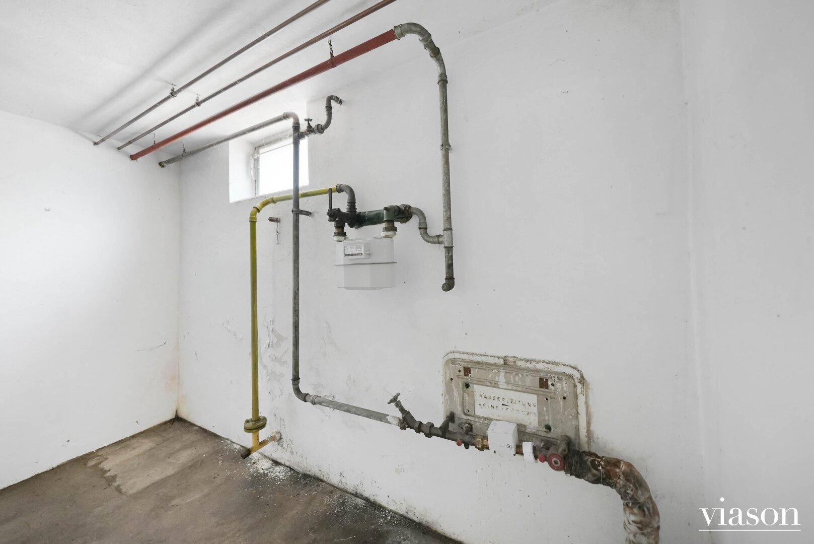 Detailansicht von Gasleitungen und Zähler in einem Kellerraum mit kleinem Fenster.
